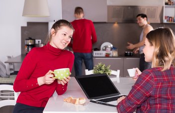 Vier Jugendliche halten sich in einer Wohnküche auf, zwei Mädchen unterhalten sich, zwei Jungs Kochen